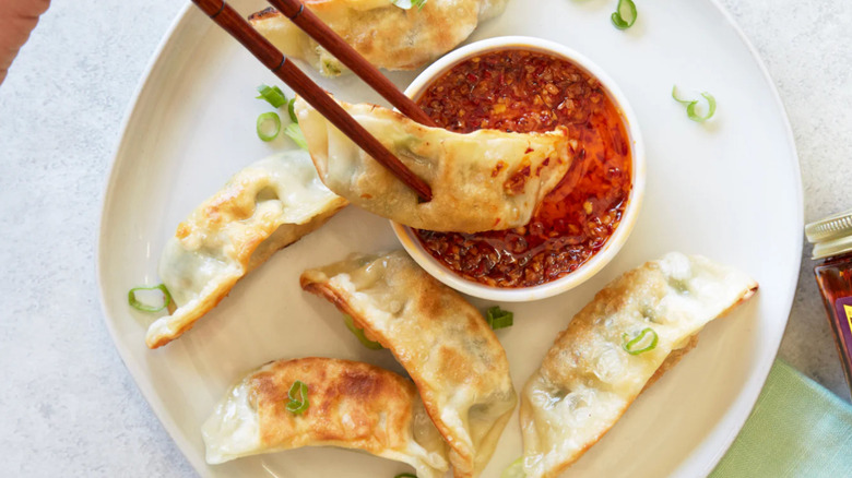 A plate of Trader Joe's potstickers with a dipping sauce and two chop sticks
