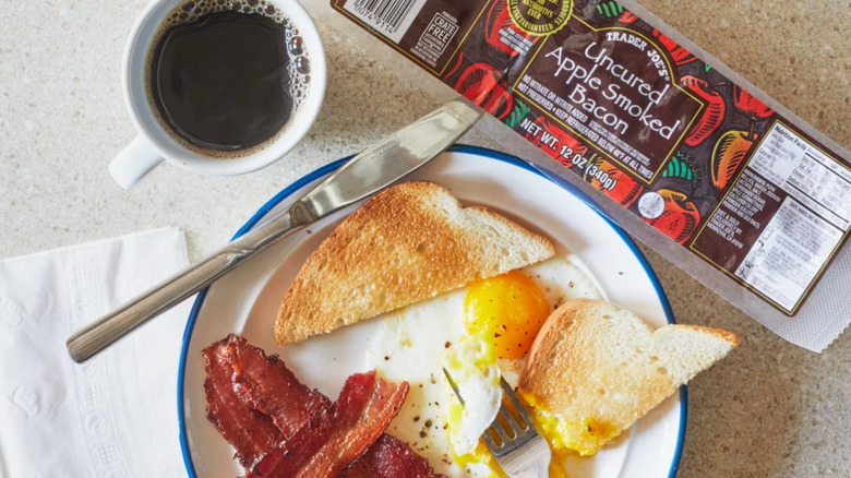 A plate of eggs, toast, bacon, and coffee next to a package of Trader Joe's Uncured Apple Smoked Bacon