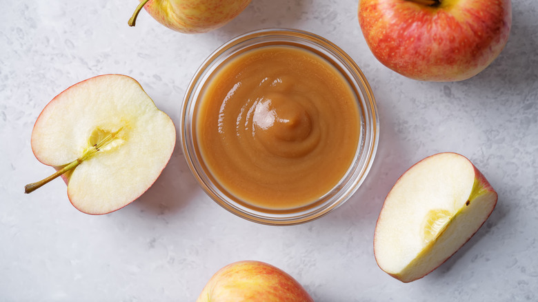 A small glass bowl of apple butter surrounded by apples