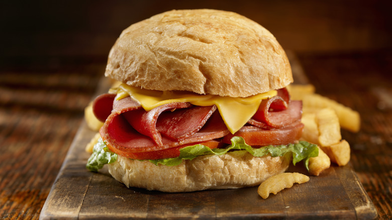 Fried bologna sandwich with cheese, bologna, tomato, and lettuce on a wooden surface