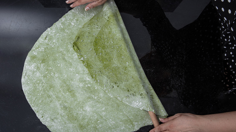 A chef rolls spinach pasta dough