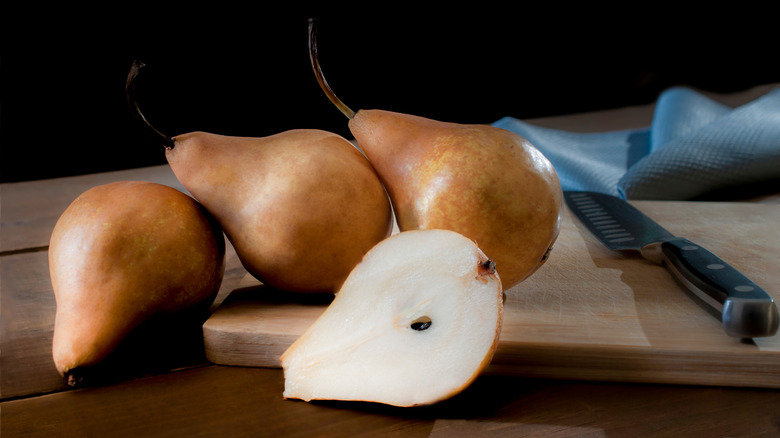 bosc pears on a wood cutting board with a knife, one pear sliced open to reveal white fruit inside