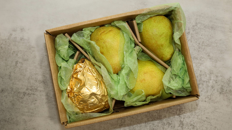 overhead shot of box of 4 comice pears, wrapped in tissue paper, one wrapped in gold foil