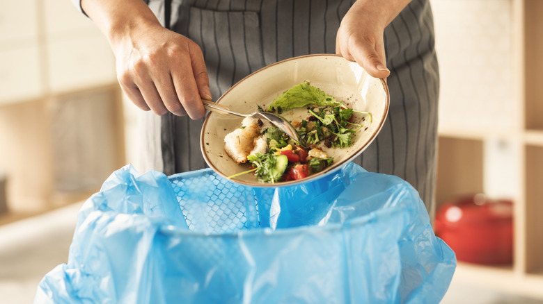 A person scrapes leftovers into a trash can