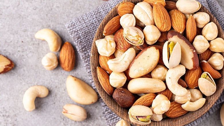 a wooden bowl with a mix of brazil nuts, cashews, almonds and other type, with some nuts spilt on the side