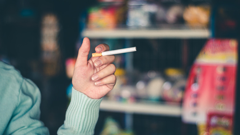 Close-up of a hand holding an unlit cigarette inside a convenience store