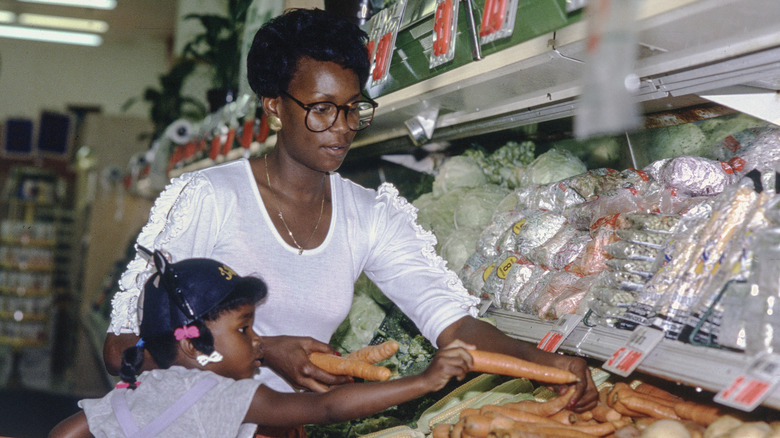 A woman and her young daughter peruse a grocery produce aisle