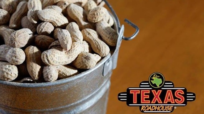 A metal bucket of uncooked peanuts are shown beside a Texas Roadhouse logo