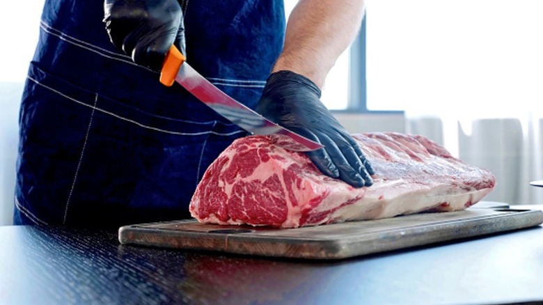A butcher cuts a large piece of beef with a knife