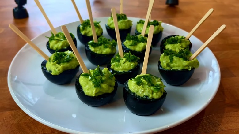 Black cauldron-style deviled eggs with green filling, chives on top, and wood food picks sticking out of them