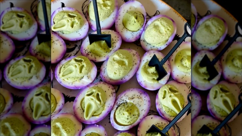 Plate of purple-webbed deviled eggs, some with molded filling and other with black shovels standing in them