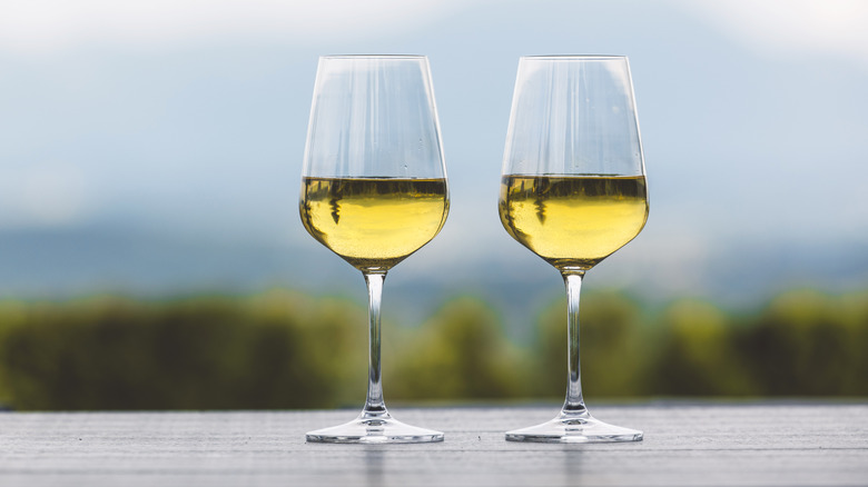 Two glasses of white wine sitting on a wooden table with a blurred nature background