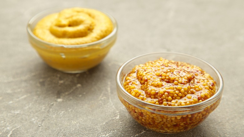Yellow mustard and grain mustard in small clear bowls