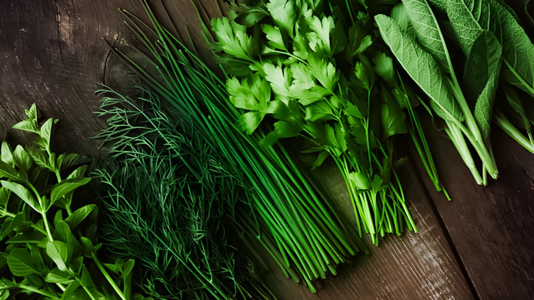Several bundles of fresh herbs are laid out against a wooden surface