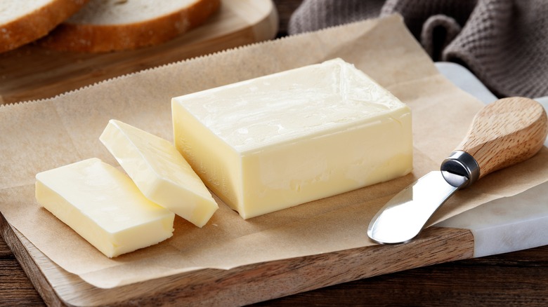 Sliced butter sitting on parchment paper on a table next to a butter knife