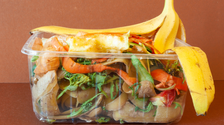 A plastic container full of vegetable scraps on a brown table