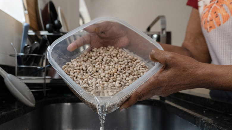 A person draining soaked beans into the sink