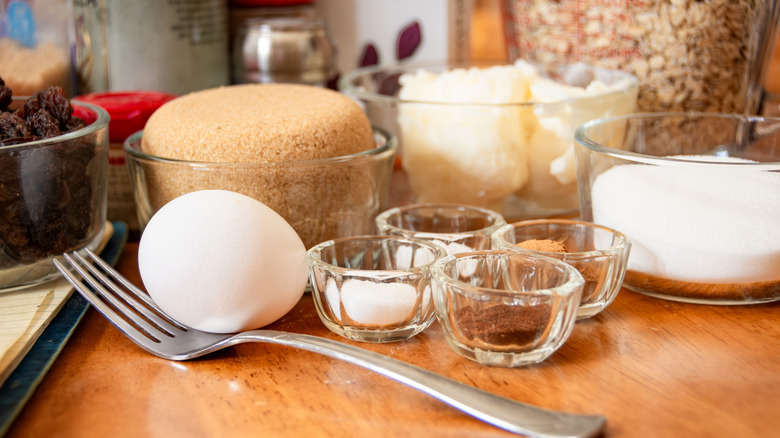A variety of baking ingredients in small glass bowls placed on a wooden table with a fork