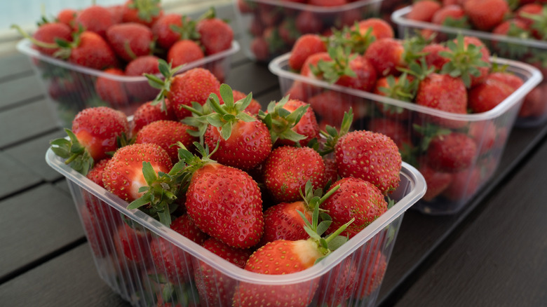 Plastic fruit containers packed with strawberries placed on a wooden table