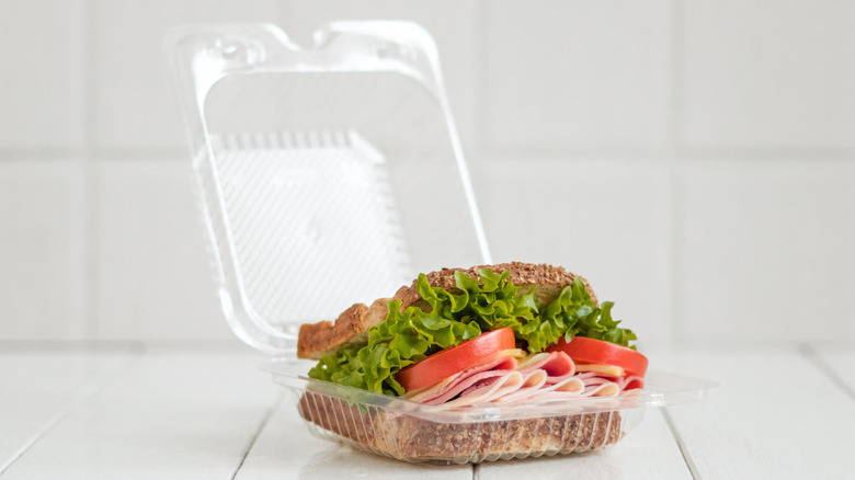 A sandwich packed in a plastic container placed on a white table