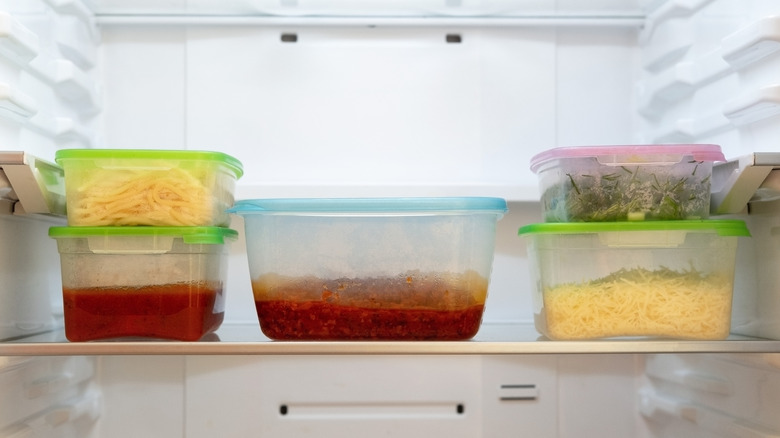 A bunch of containers packed with leftovers stacked inside a refrigerator
