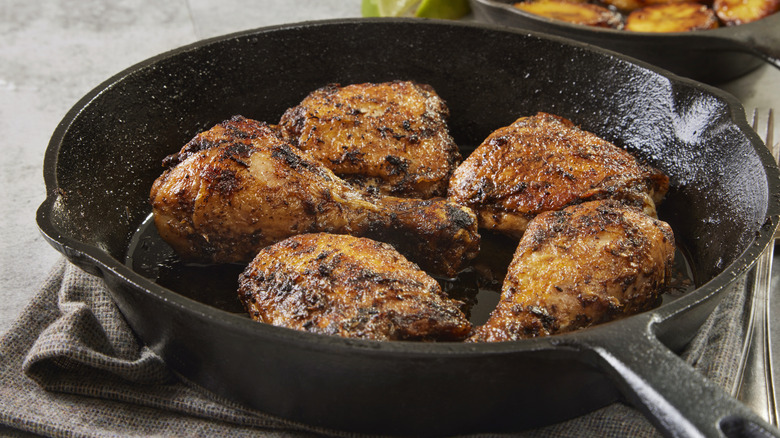 Jerk style chicken thighs cooking in a black cast iron skillet