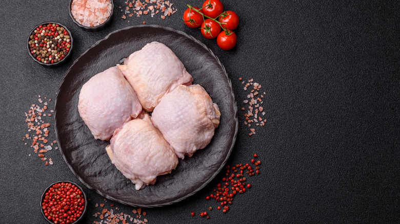Raw chicken thighs sit on a black plate after being pat dry