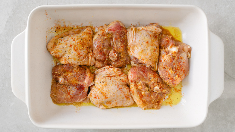 Seasoned chicken thighs sit in a white casserole dish