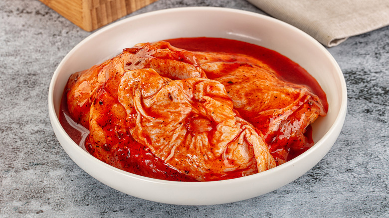 Chicken thighs with skin on them sit in a bowl of bright red marinade