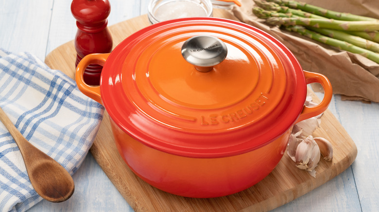 A red Dutch oven on a wooden board placed on a white table