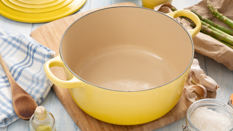An empty yellow Dutch oven on a wooden board