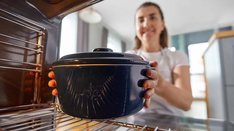 A woman putting a Dutch oven inside a hot oven