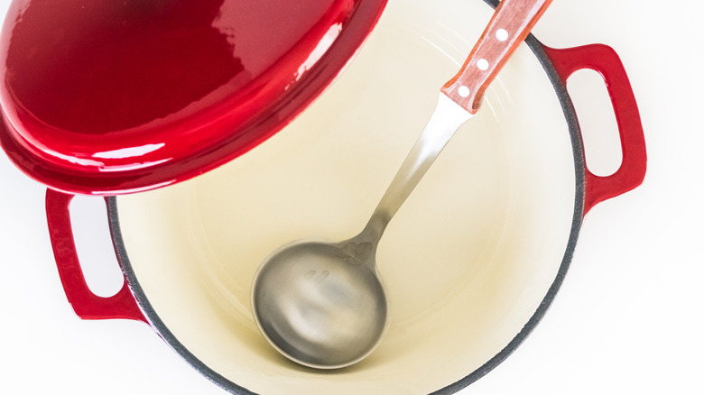 An empty Dutch oven with a stainless steel ladle on a white table