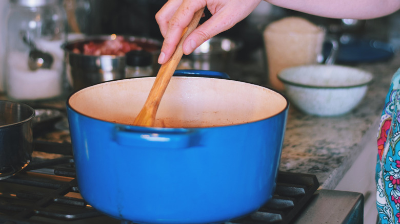 A person cooking food in a Dutch oven on a stovetop