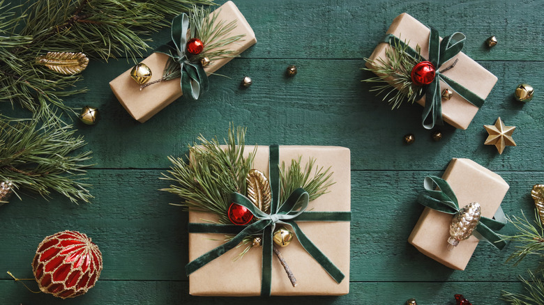 An assortment of wrapped gifts with bows, surrounded by pine needles and winter ephemera