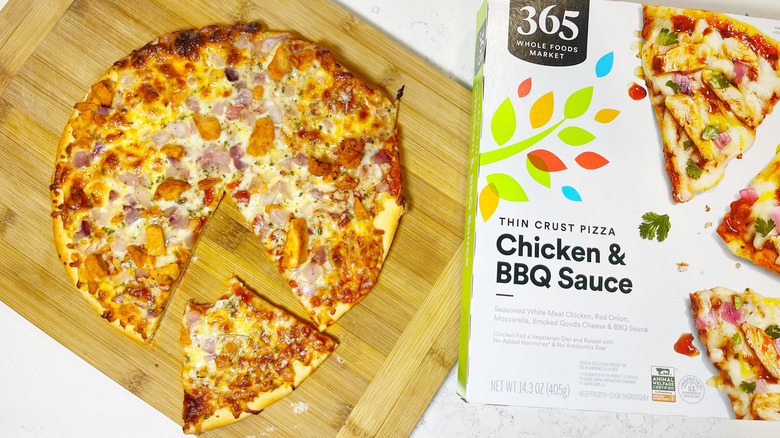 The chicken and BBQ sauce pizza with a slice out of it on a cutting board next to the box