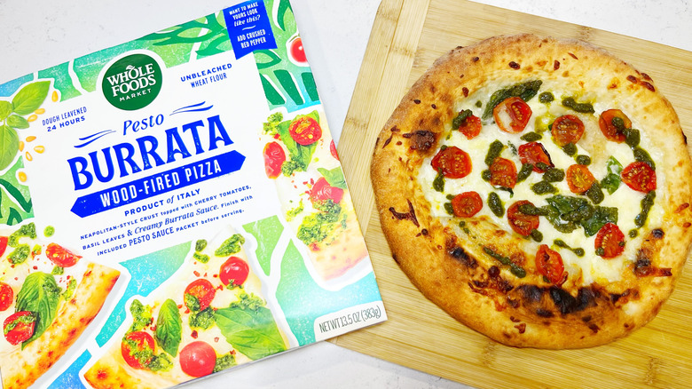 The pesto burrata pizza on a cutting board next to the box