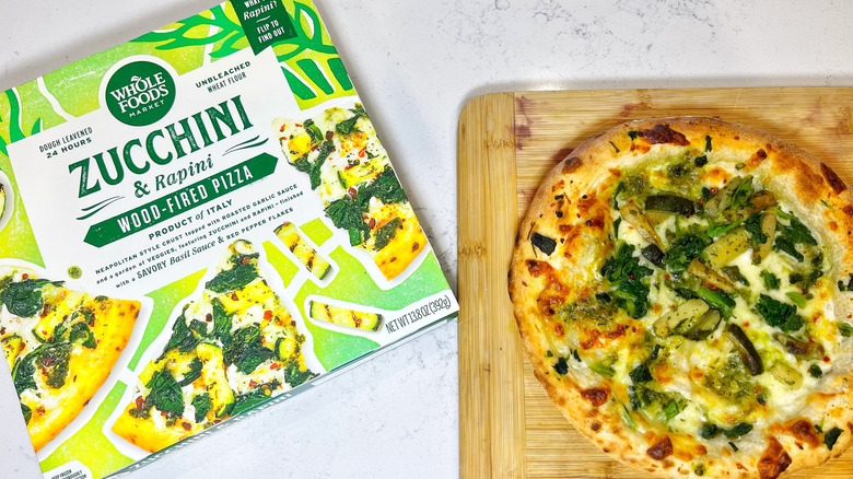 The zucchini and rapini pizza box next to the pie on a cutting board