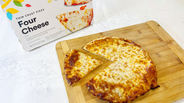 The four cheese pizza on a cutting board with the box behind it