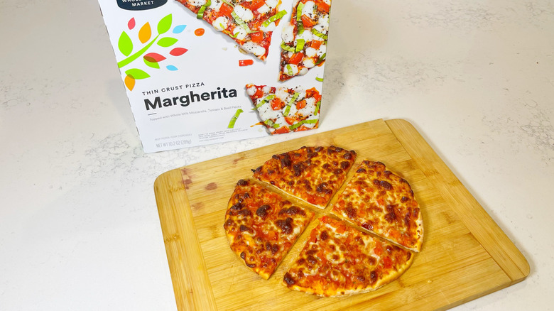 The margherita pizza cut into four slices on a cutting board with the box behind it