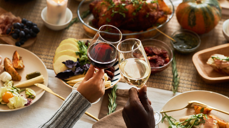 Two people clinking glasses of red and white wine at Thanksgiving meal