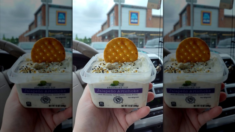 Hand holding jalepeno artichoke dip in front of Aldi store