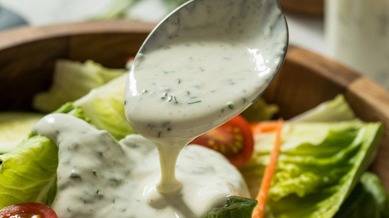 Ranch dressing being spooned onto a salad with lettuce, tomato, and carrots