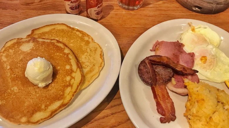 A breakfast combo meal from Cracker Barrel with pancakes, eggs, hashbrowns, and meat on white plates