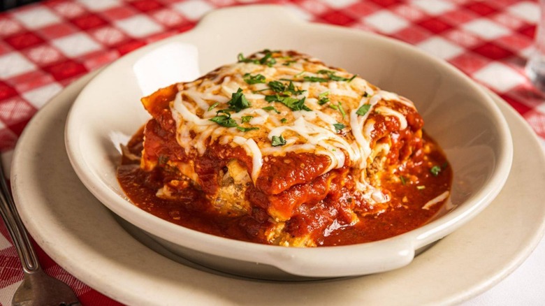 A close-up of lasagna in a white dish on a red checkered tablecloth at Maggiano's Little Italy