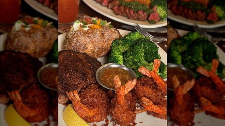 A close-up of a dinner plate with steak, coconut shrimp, a loaded baked potato, and broccoli
