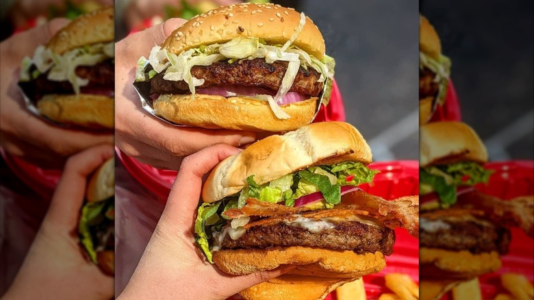 Two hands holding large Red Robin burgers with toppings