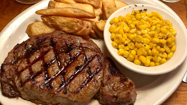 A ribeye steak with corn and fries on a large white platter from Texas Roadhouse