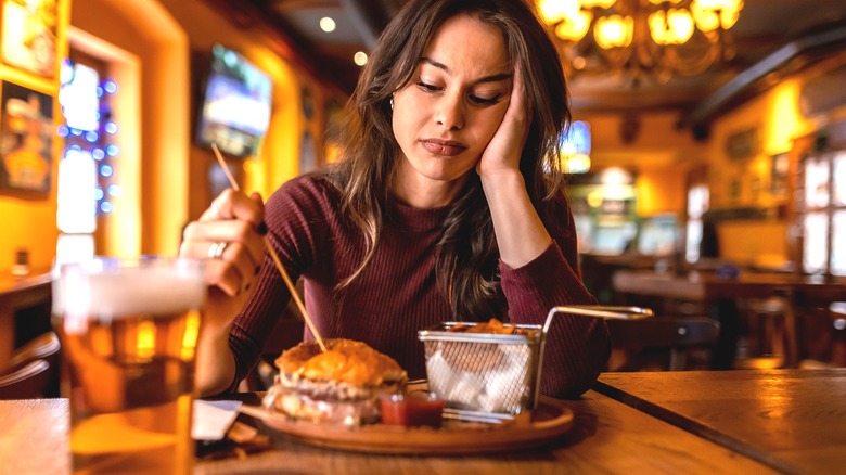 woman in restaurant looking unhappily at the burger in front of her