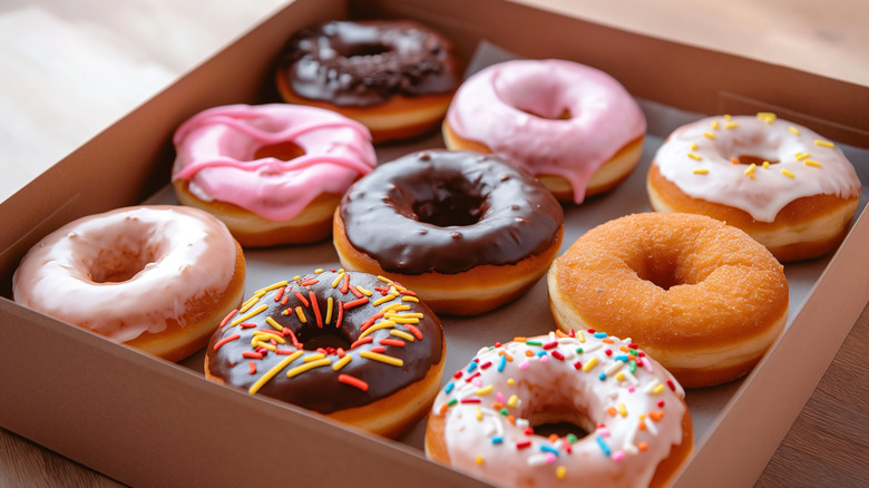 A selection of colorful glazed and unglazed ring donuts, arranged in a box